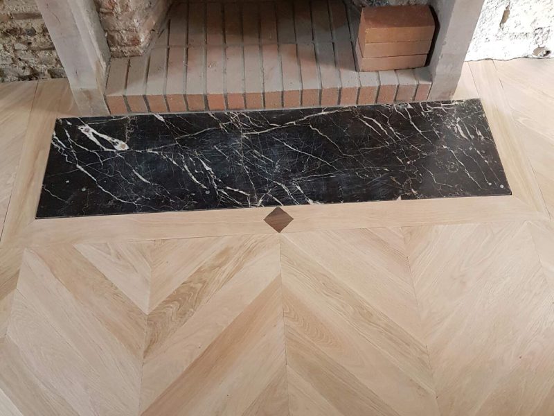 Photo d'une cheminée montrant la réalisation d'une pose de parquet avec l'incrustation d'une dalle devant la cheminée et d'un ornement entre la jonction des deux - pose en point de Hongrie