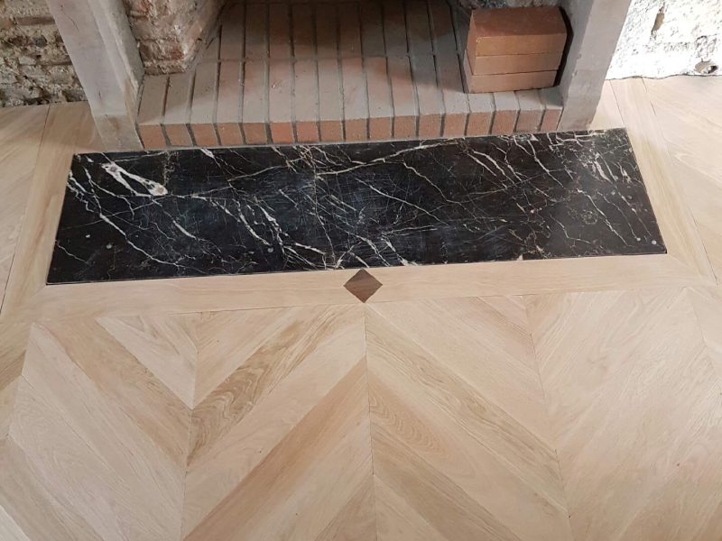 Photo d'une cheminée montrant la réalisation d'une pose de parquet avec l'incrustation d'une dalle devant la cheminée et d'un ornement entre la jonction des deux - pose en point de Hongrie