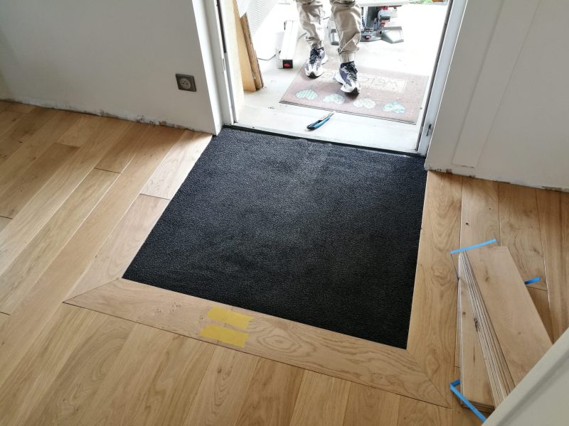 Photo d'une entrée montrant la réalisation d'une pose de parquet avec intégration d'un tapis d'entrée - pose traditionnelle à l'Anglaise